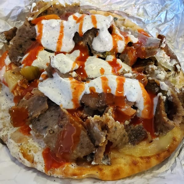 King Of Gyros' Greek gyro, topped with white tzatziki sauce and red hot sauce, on pita bread.