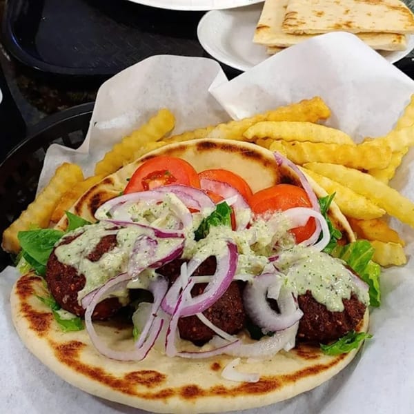 King Of Gyros falafel pita with tomatoes, onions, lettuce, tzatziki sauce, and a side of fries.
