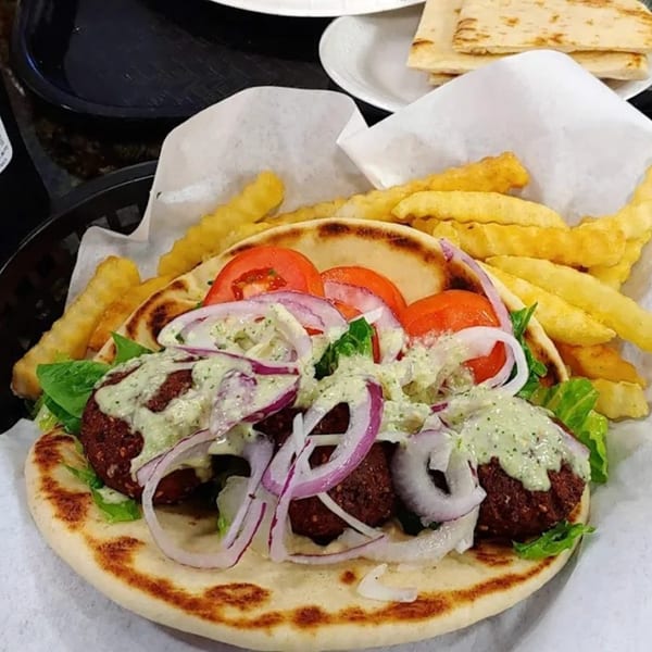King Of Gyros falafel pita with lettuce, tomatoes, red onions, tzatziki sauce, and fries.