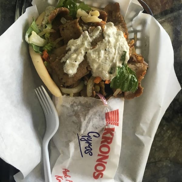 A King Of Gyros gyro with meat, lettuce, onions, and tzatziki sauce, served in a paper wrapper.