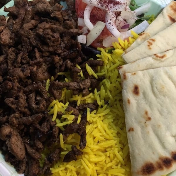 King Of Gyros plate with sliced meat, yellow rice, pita bread, and a side salad.