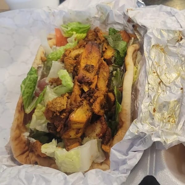 A King Of Gyros chicken gyro with lettuce and tomatoes in a white paper wrapper.