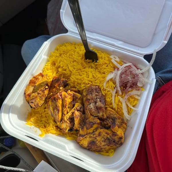 A King Of Gyros chicken and rice platter with onions and a fork in a white takeout container.