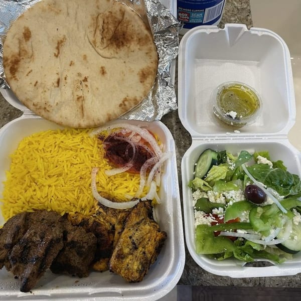 Greek meal with yellow rice, grilled meat, pita bread, and a side salad in takeout containers.