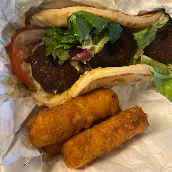 King Of Gyros falafel pita with lettuce, tomato, sauce, and two fried cheese sticks.