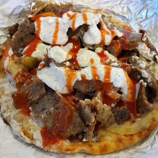 King Of Gyros' Greek gyro meat and toppings with white tzatziki and red hot sauce on pita bread.