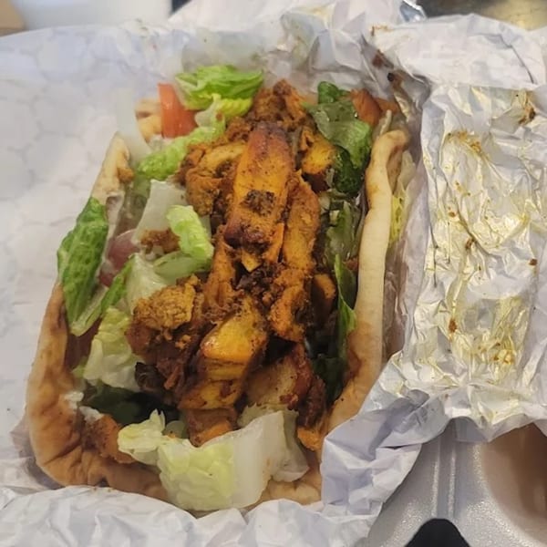 King Of Gyros chicken gyro with lettuce and tomatoes, served in white paper.