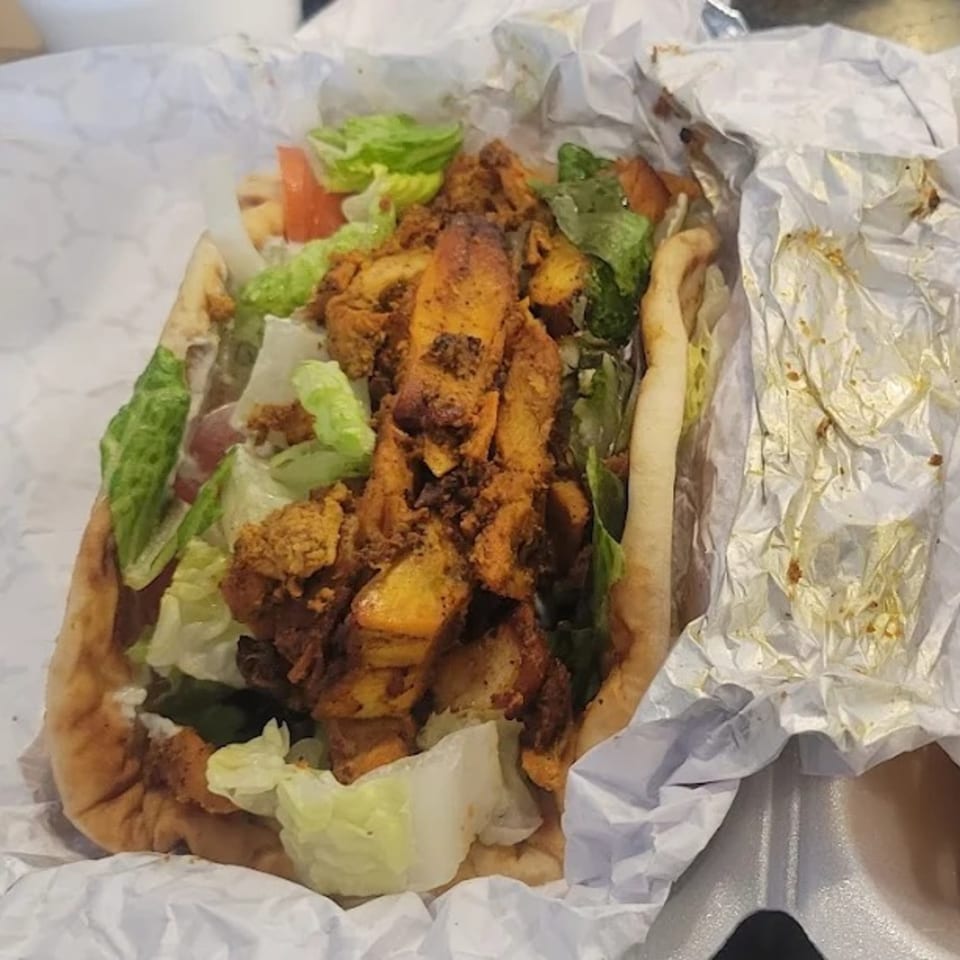 King Of Gyros chicken gyro with lettuce and tomatoes, served in white paper.