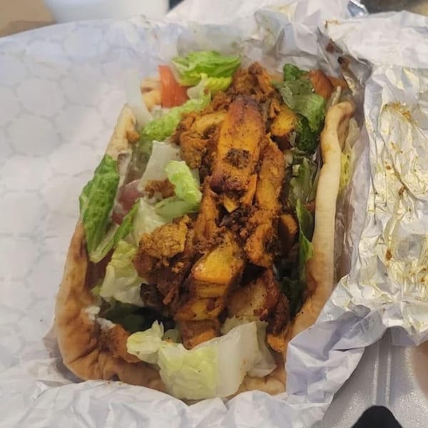 King Of Gyros chicken gyro with lettuce and tomatoes in a white paper wrap.