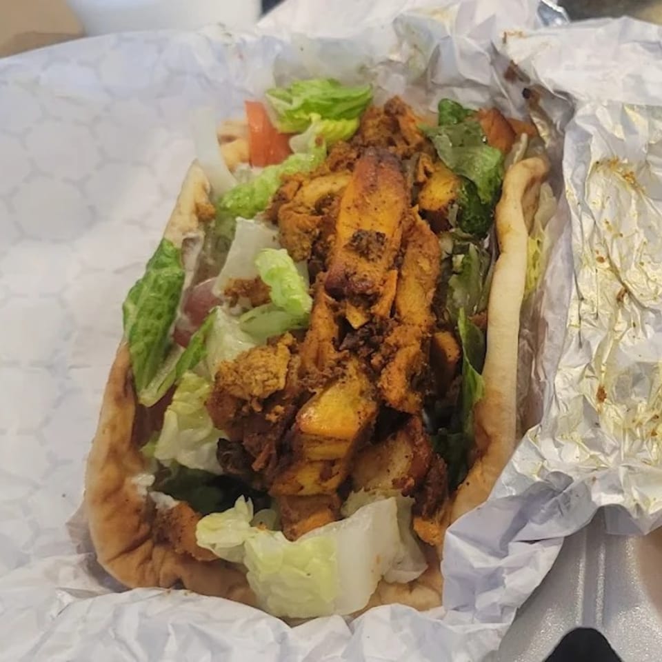 King Of Gyros chicken gyro with lettuce and tomatoes in a white paper wrap.