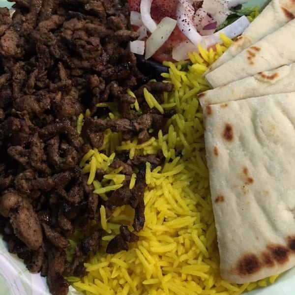 King Of Gyros' Greek platter with sliced meat, yellow rice, pita bread, and a side salad.