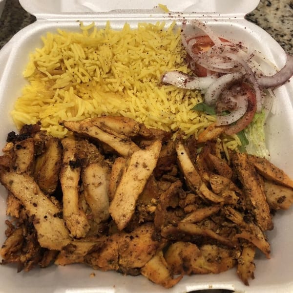 King Of Gyros chicken shawarma plate with yellow rice, onions, tomatoes, and lettuce in a styrofoam container.